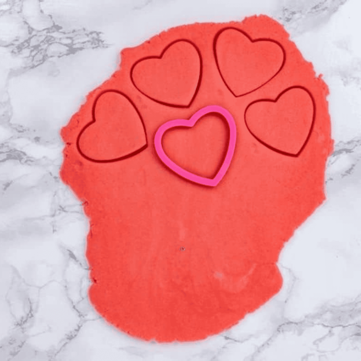Rolling out red and pink dough and cutting heart shapes with cutter.