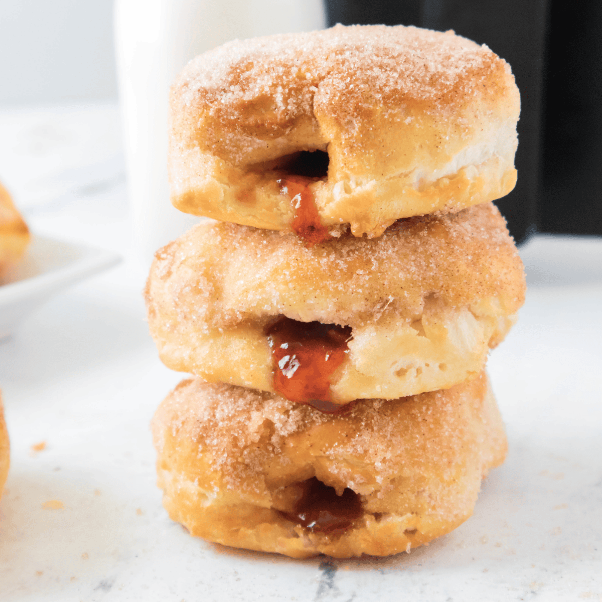 Stack of air fryer jelly donuts with strawberry jam oozing from the center, coated in cinnamon sugar