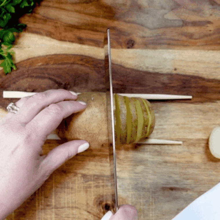 Slicing potatoes thinly for Hasselback style using chopsticks or wooden spoons to avoid cutting through completely