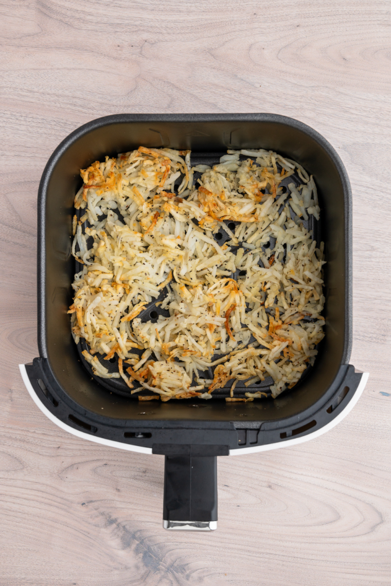 Shredded hash browns cooking in air fryer at 375°F while being stirred halfway through for even crispiness and golden browning