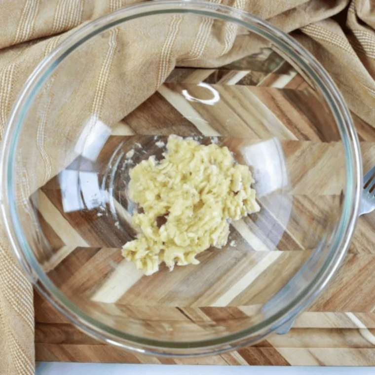 Ripe banana mashed with a fork in a small white bowl until smooth