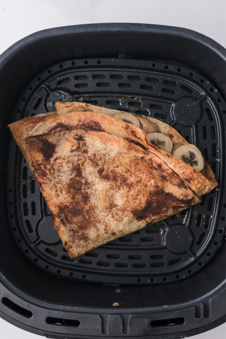 Cooked banana Nutella quesadilla in an air fryer basket with golden blistered spots on the tortilla