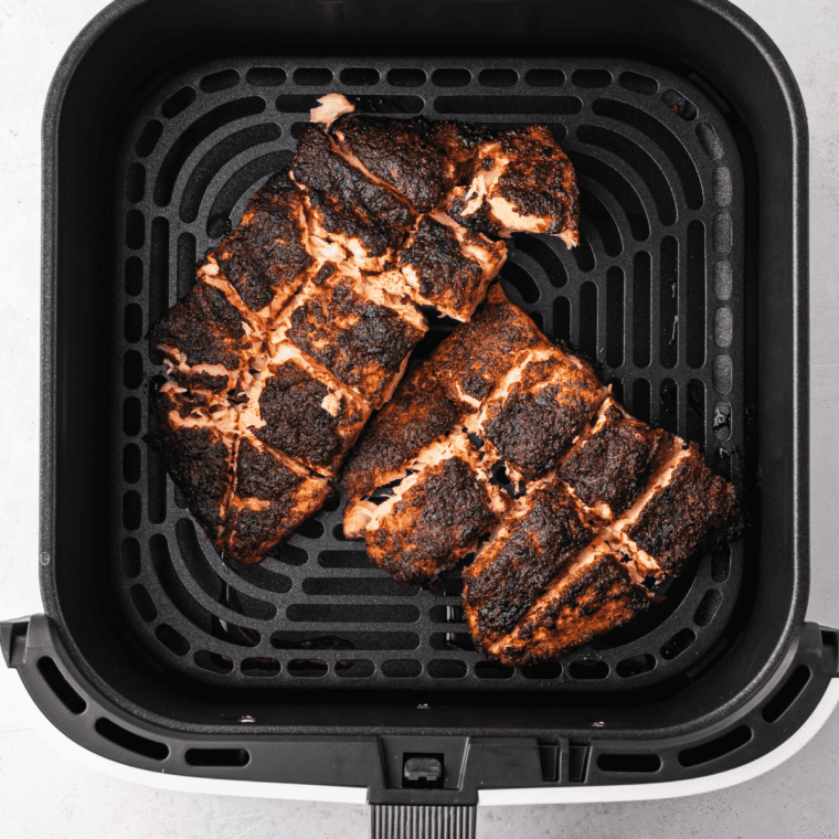 Blackened salmon fillets cooking in the air fryer basket until flaky and crisp