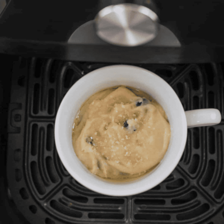 Pouring blueberry mug cake batter into sprayed ramekins, topped with sparkling sugar, ready for air fryer