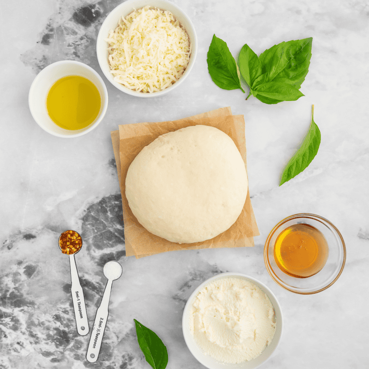 Pizza dough, melted butter, parmesan and seasonings on a marble table