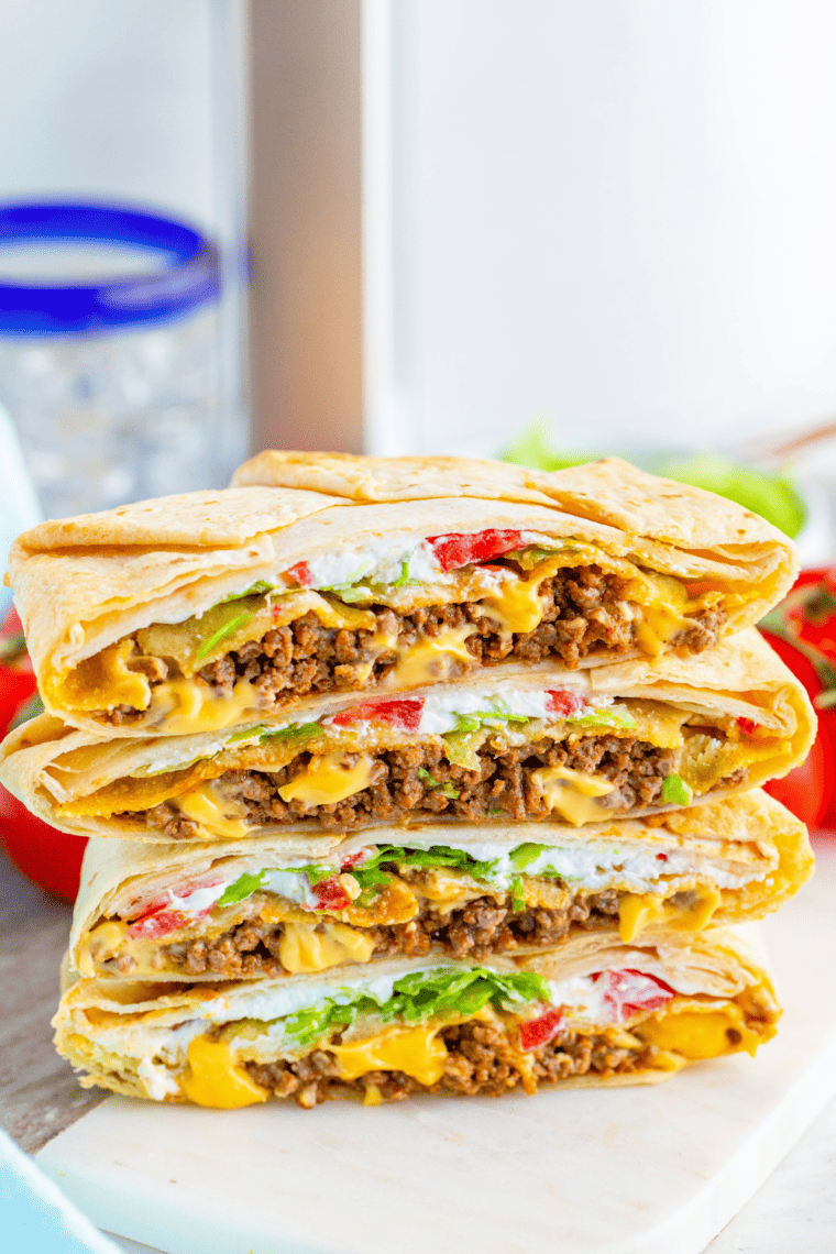 Homemade crunchwrap supreme on plate cut in half revealing beef, nacho cheese, lettuce, and crunchy tostada layer.