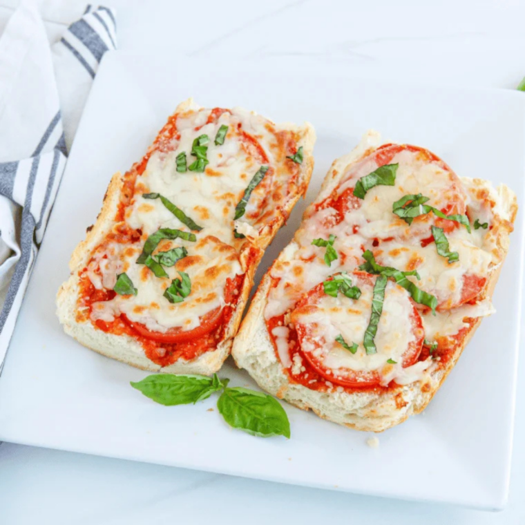 Sliced air fryer French bread pizza with melted mozzarella and fresh basil on a wooden cutting board