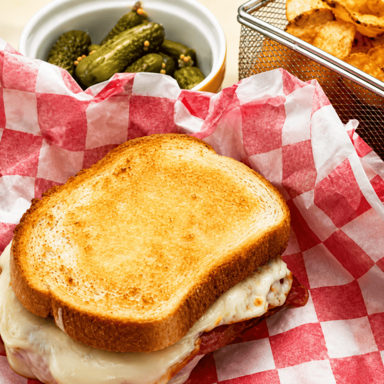 Air fryer Italian grilled cheese sandwich cut in half on a white plate, showing melted provolone, salami and prosciutto