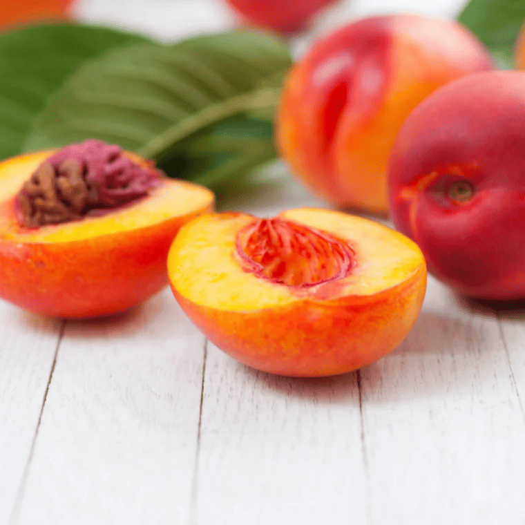 Fresh ingredients for air fryer grilled nectarines arranged on a wooden surface, including ripe nectarines, melted butter, brown sugar, ground cinnamon, vanilla extract, lemon, and a pinch of salt.
