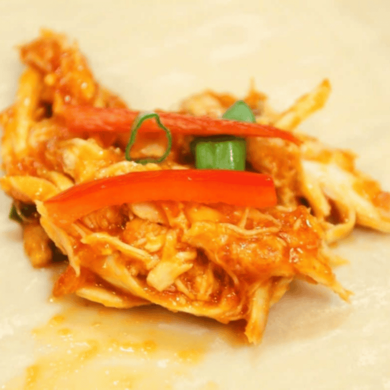 Egg roll wrapper filled with chicken mixture, red bell pepper slices, and scallions before rolling.