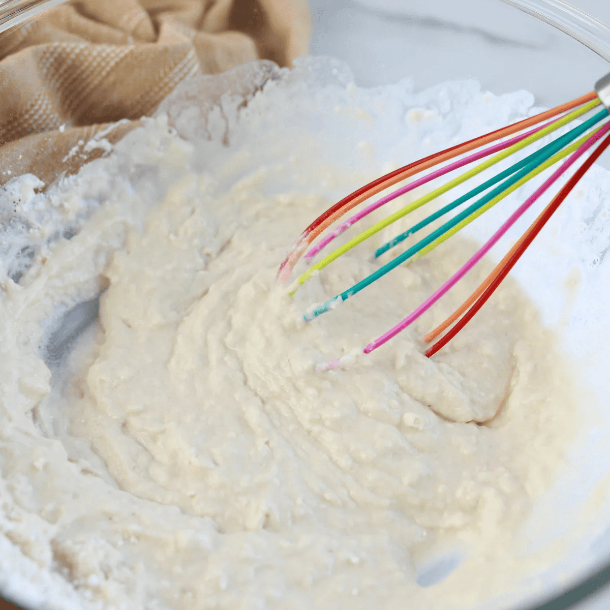 Pancake batter being mixed in a large bowl with pancake mix, milk, eggs, butter, and vanilla extract.