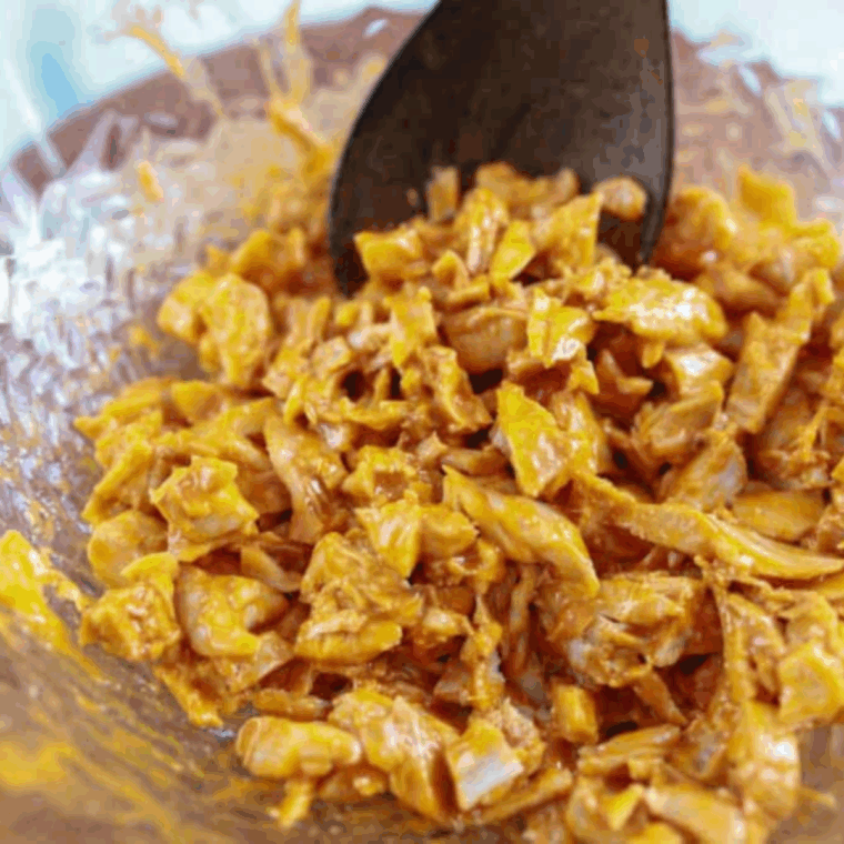 Shredded chicken coated in spicy buffalo sauce in a large mixing bowl