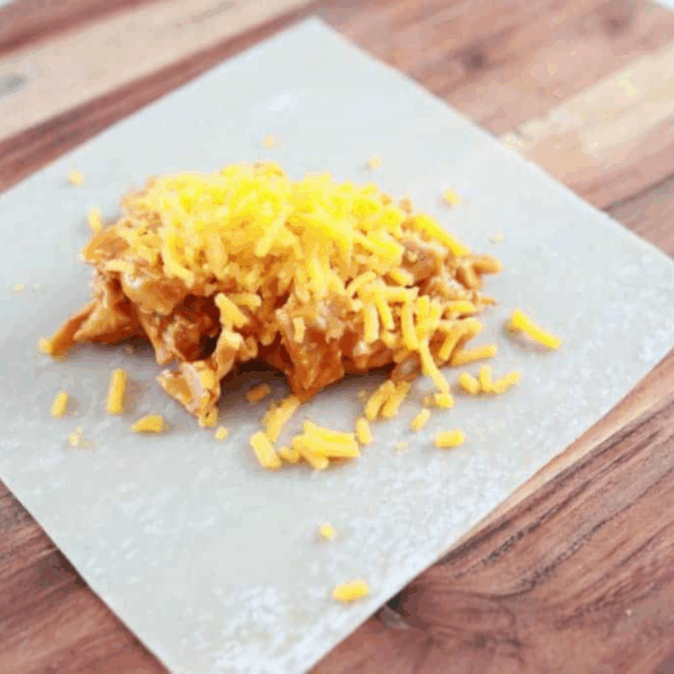 Egg roll wrapper on cutting board with buffalo chicken filling in center, ready to roll