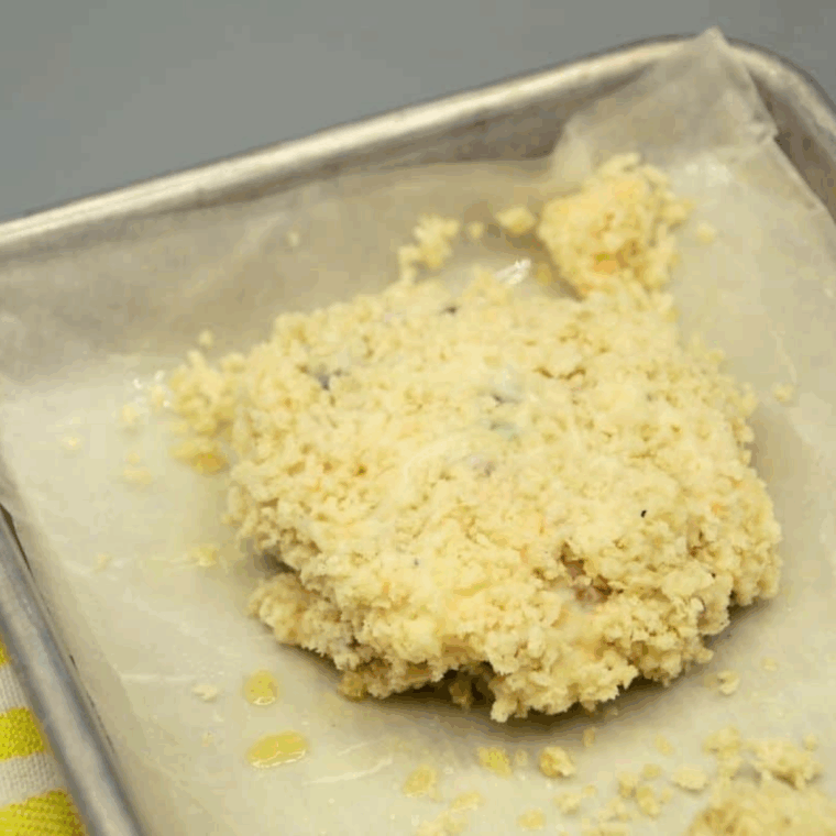 Eight panko-coated potato pancakes lined up on a parchment-paper-lined plate ready for the freezer.