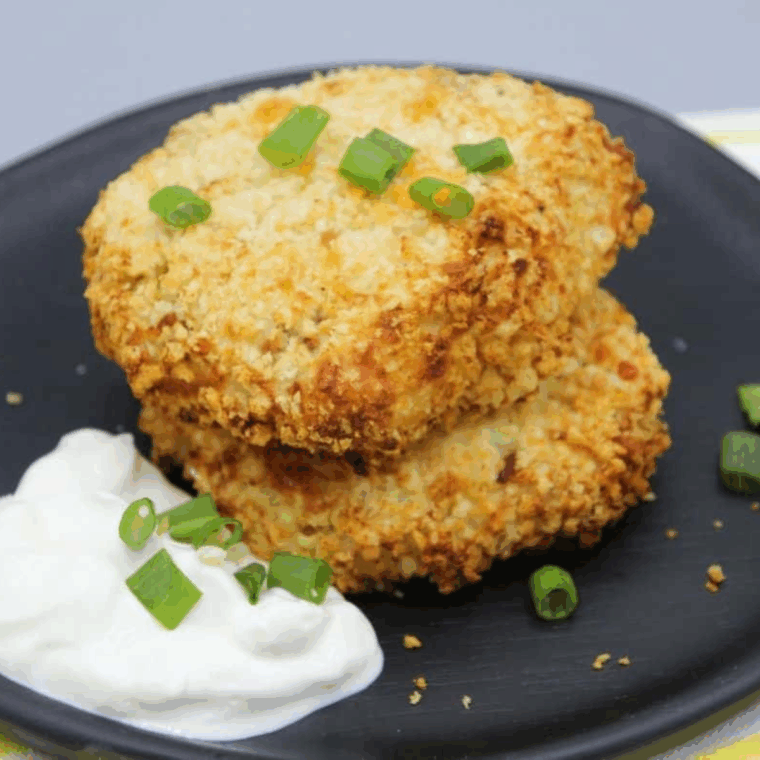 Two air fryer mashed potato pancakes topped with sour cream, chopped scallions, and crumbled bacon on a blue ceramic plate.