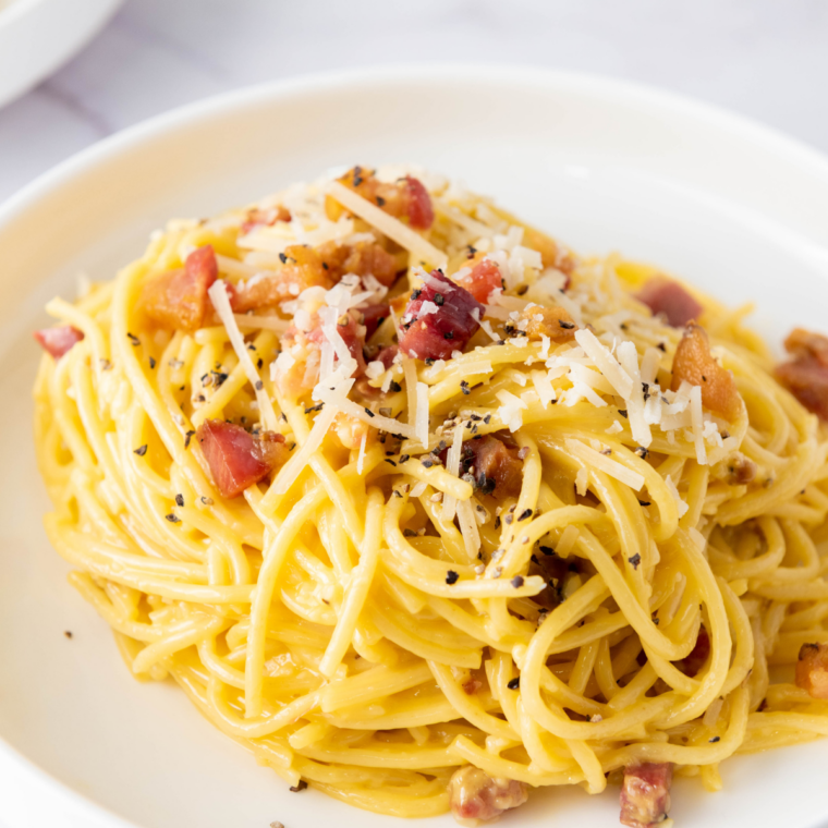 Slimming World friendly Spaghetti Carbonara served in a white bowl with crispy bacon, creamy sauce, and sprinkled parsley.