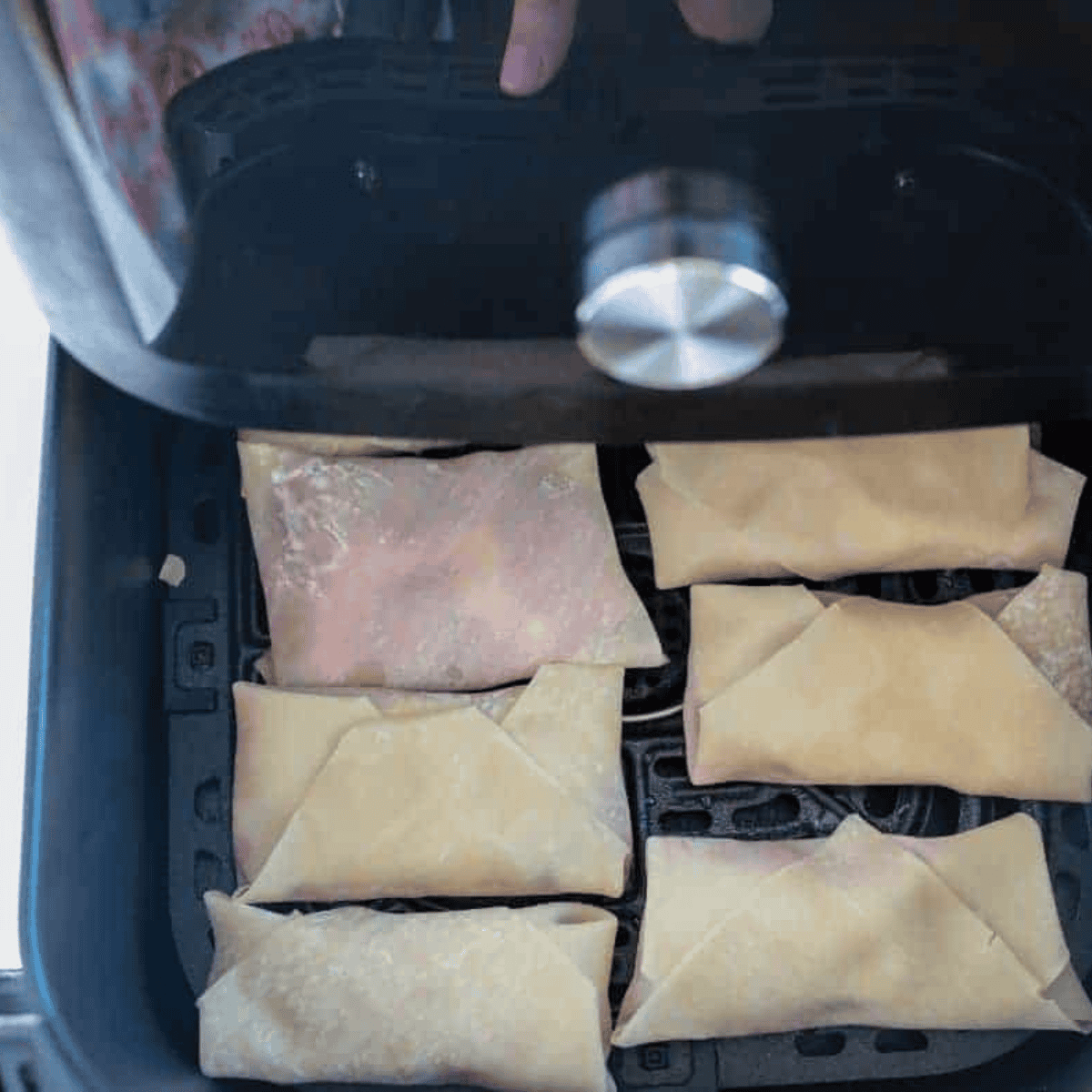Folding and rolling egg roll wrapper over cheesecake and cherry filling, sealing edges with water to prevent leakage.