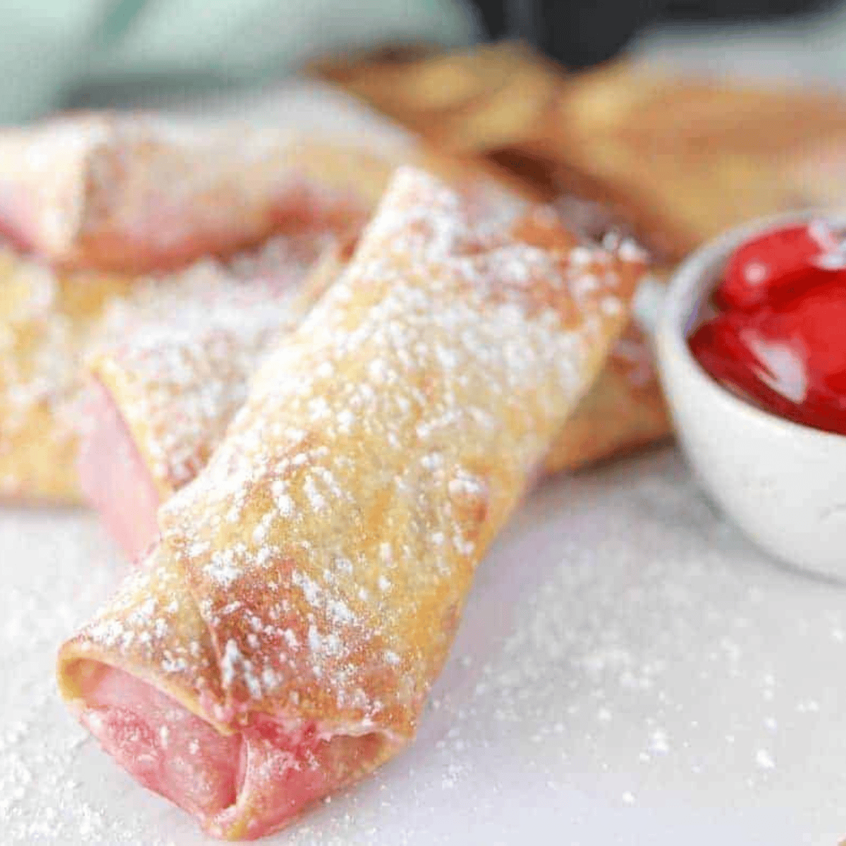 Golden air fryer cherry cheesecake egg rolls with melted cherry and cream cheese filling, served on a plate.
