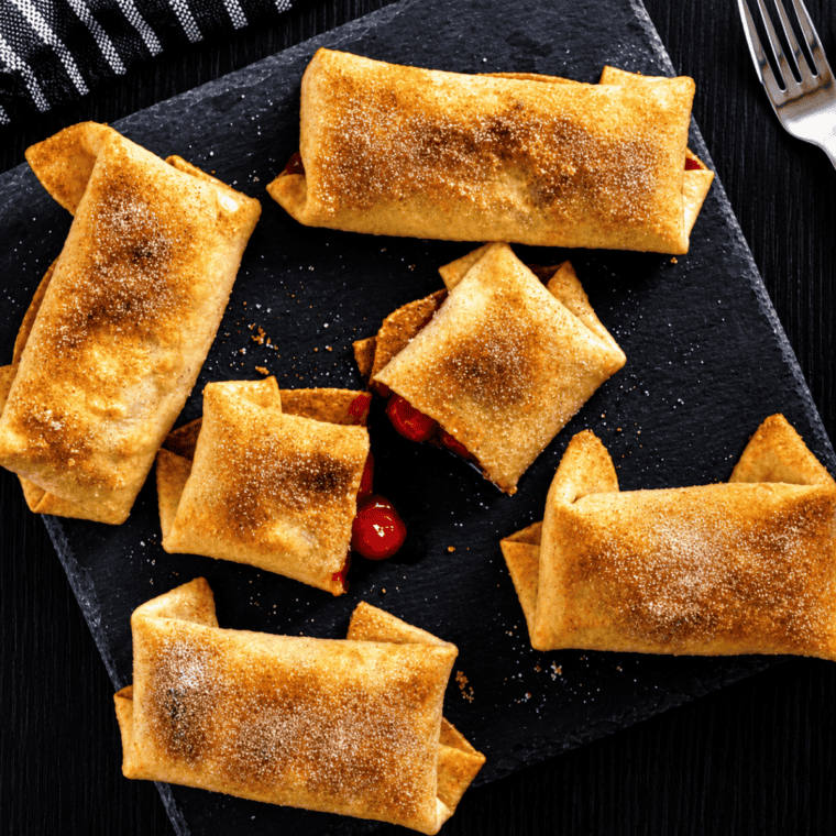 Air fryer cherry chimichangas on a white plate, dusted with cinnamon sugar and served with vanilla ice cream