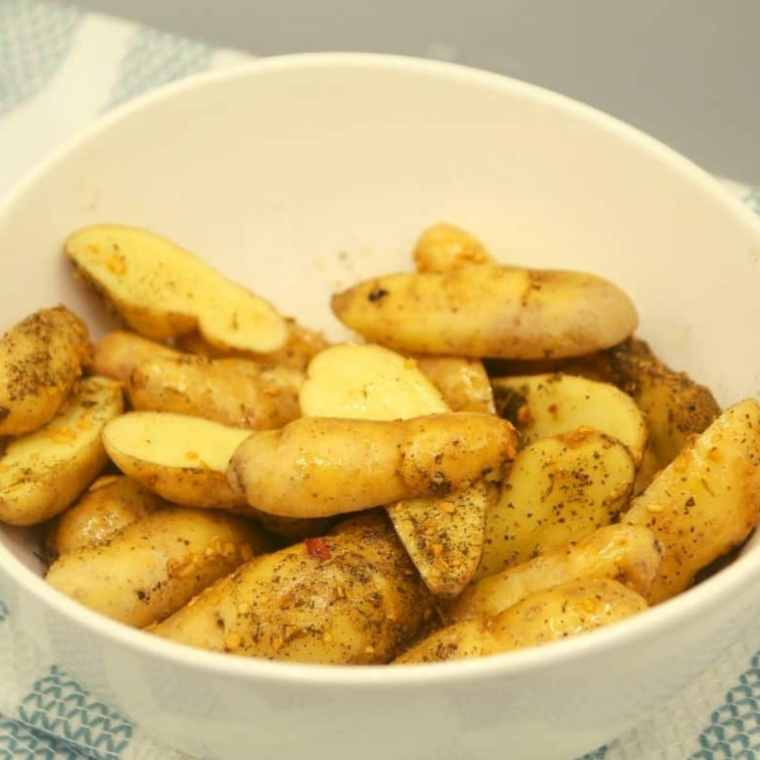 Fingerling potatoes halved lengthwise on a cutting board beside minced garlic and dried herbs