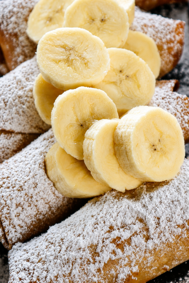 Crispy peanut butter banana egg rolls garnished with sliced bananas and powdered sugar