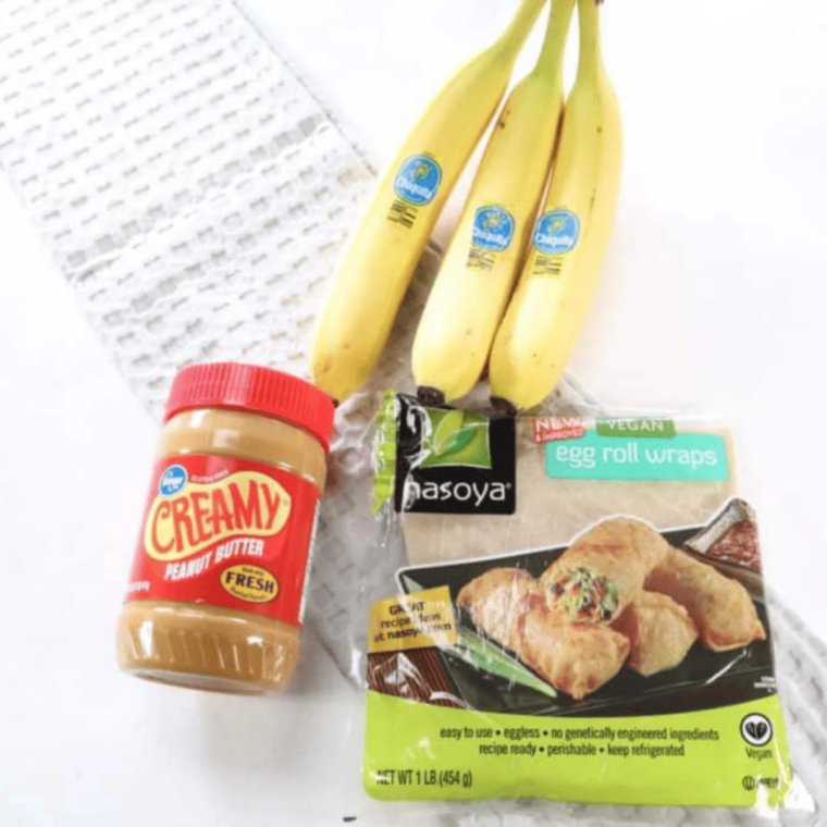 Egg roll wrappers, creamy peanut butter, and ripe bananas laid out on a counter