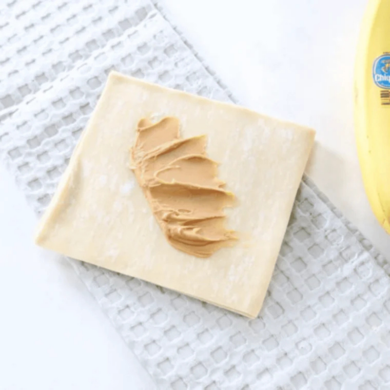 Peanut butter spread in a thin band across the center of an egg roll wrapper