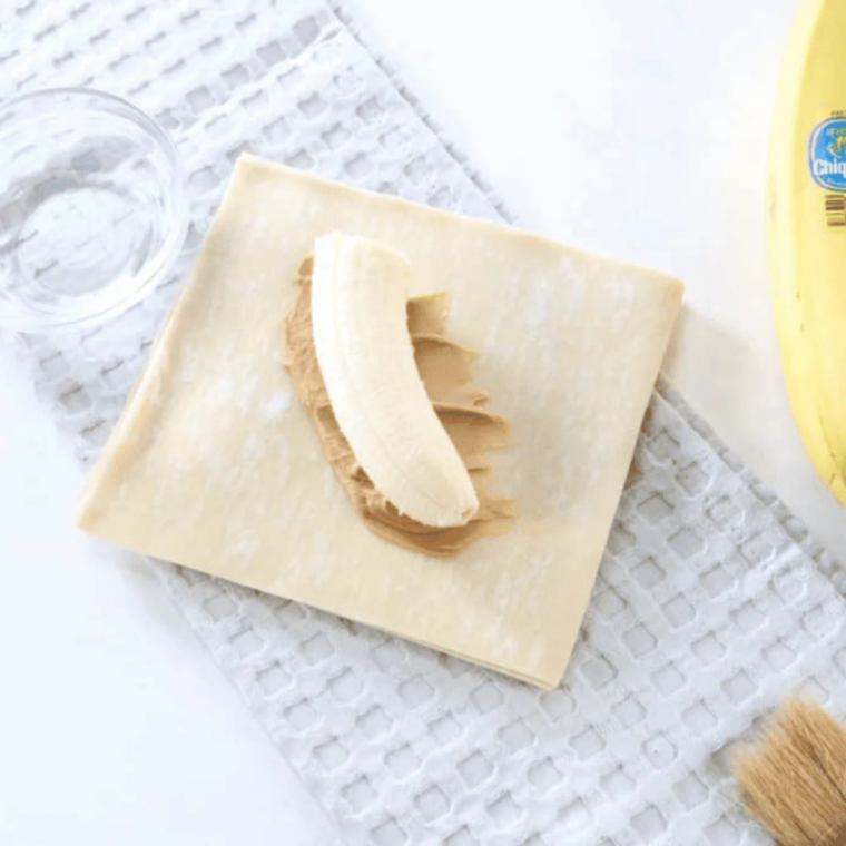 Half a banana placed on peanut butter with the egg roll wrapper edges brushed with water