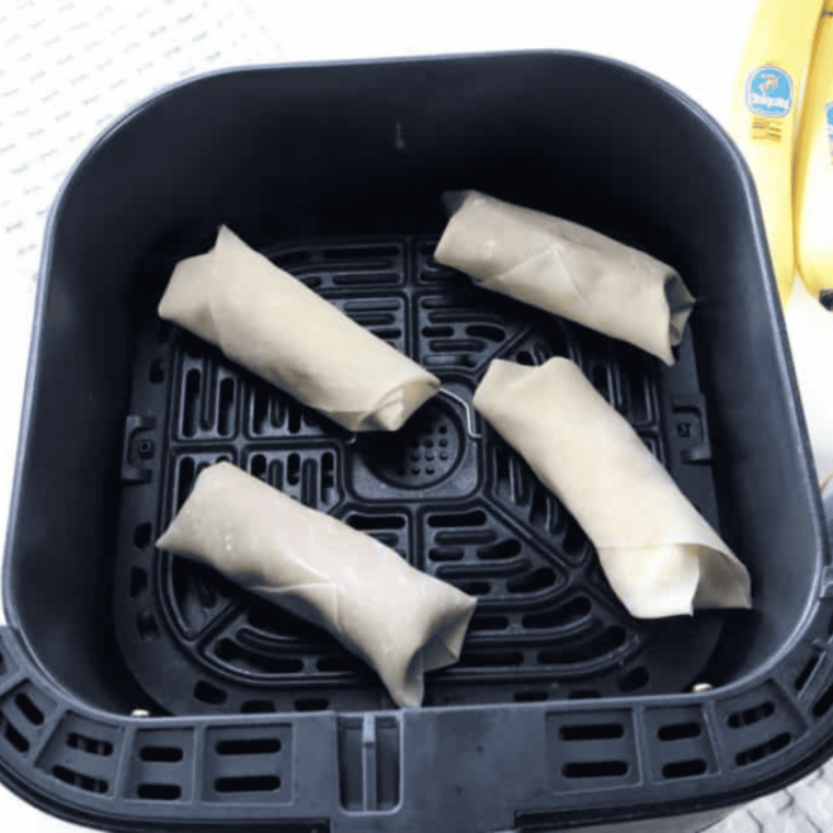 Sealed peanut butter banana egg rolls arranged seam-side down in an air fryer basket