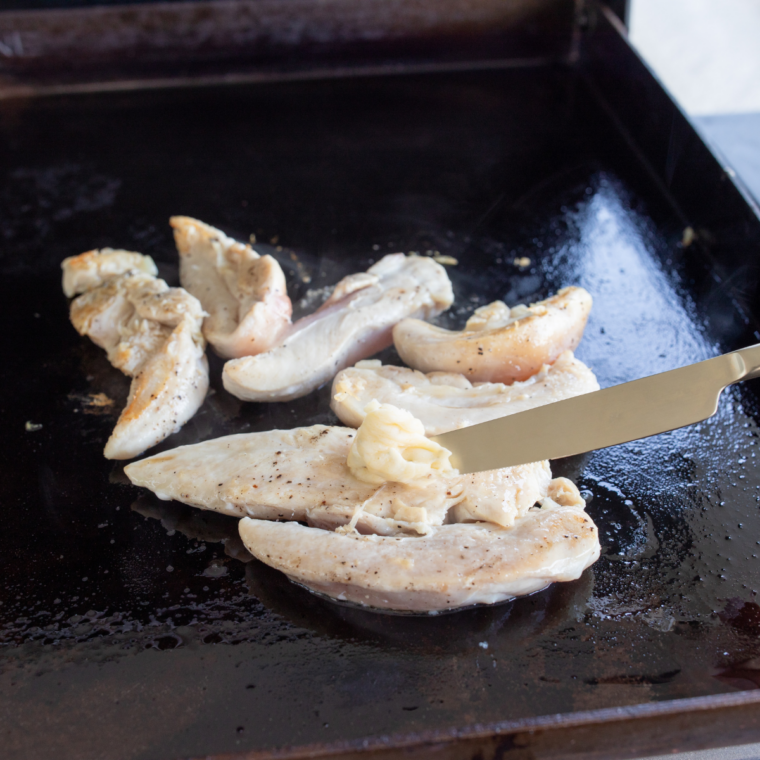 Seasoned chicken tenders searing on a hot Blackstone griddle for mojo chicken tacos.