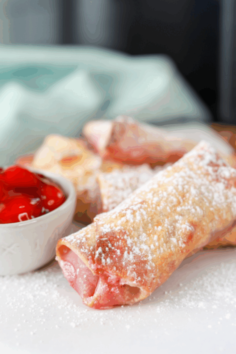 Golden air fryer cherry cheesecake egg rolls on a plate, crispy outside, creamy cherry-filled center.