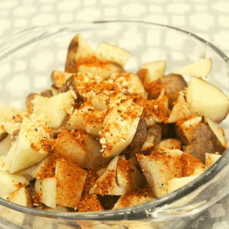 Diced potatoes tossed with oil and seasonings in a large bowl