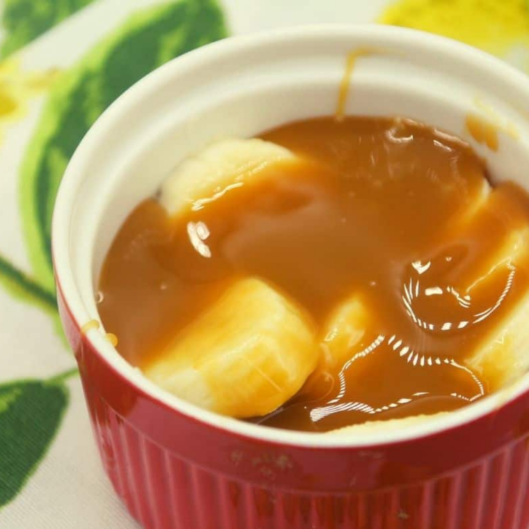 Caramel sauce drizzled over sliced bananas in a ramekin before air frying