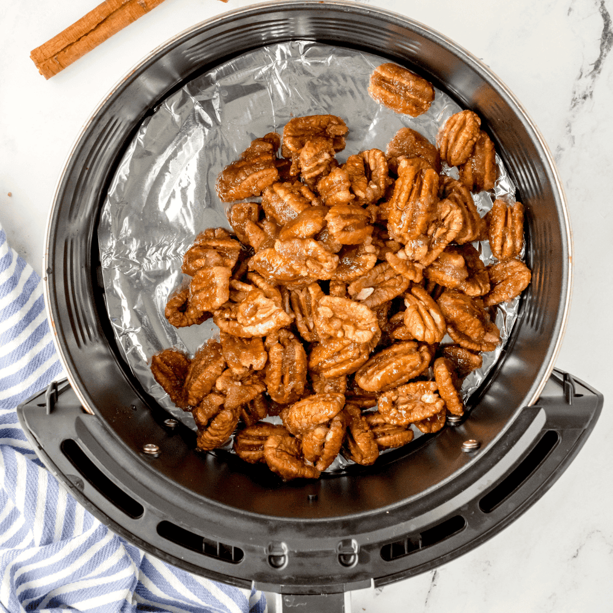 Pecan mixture spread in a single layer in the air fryer basket, ready to cook.