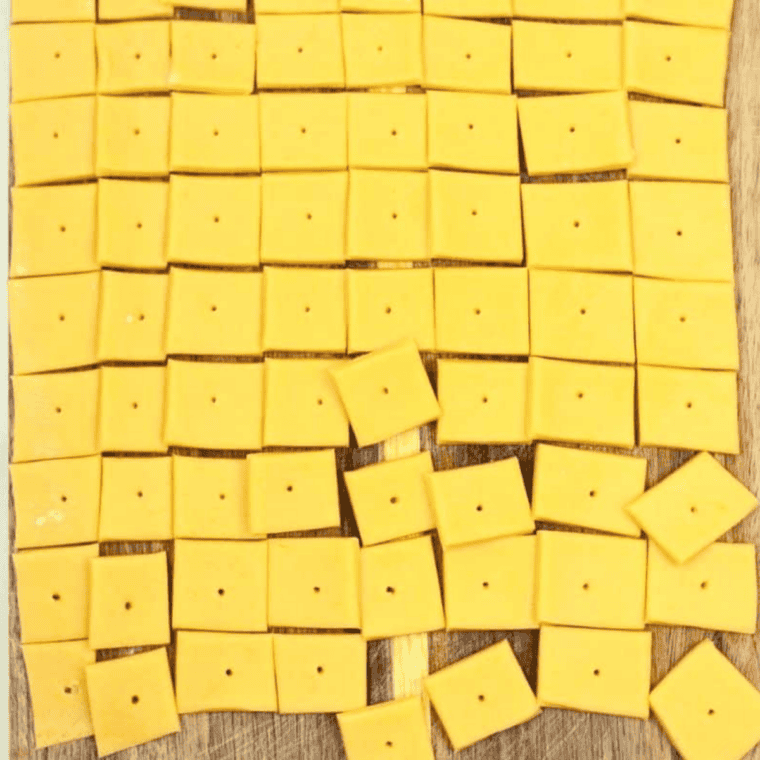 Cheddar cracker dough cut into small squares with a hole poked in each center