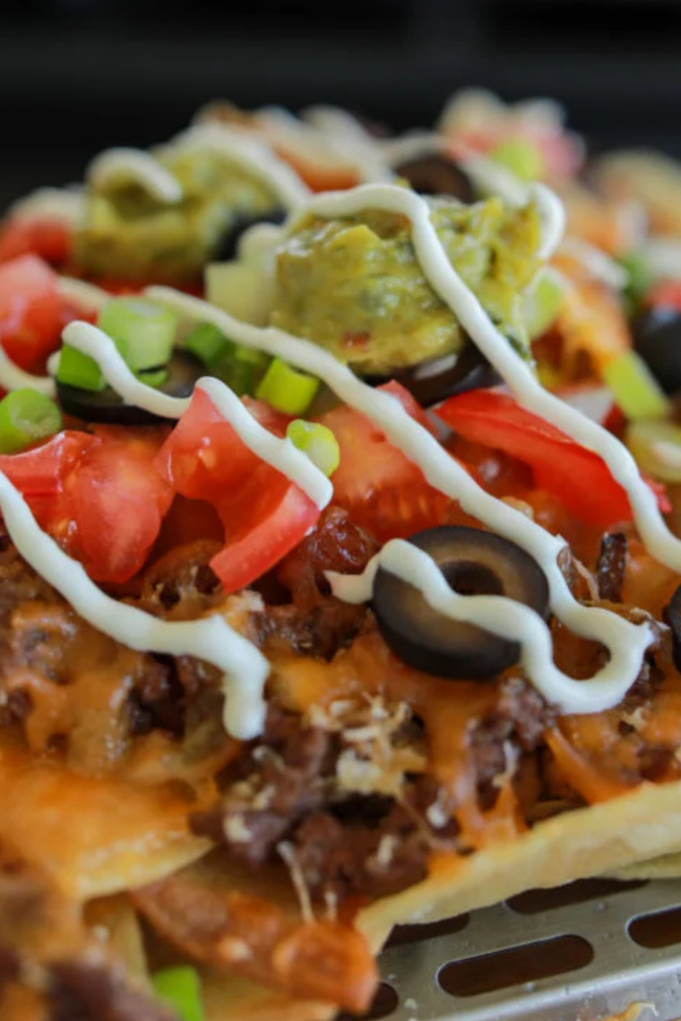 Griddle-made nachos piled high with beef, cheese, jalapeños, olives, and salsa on a Blackstone flat top