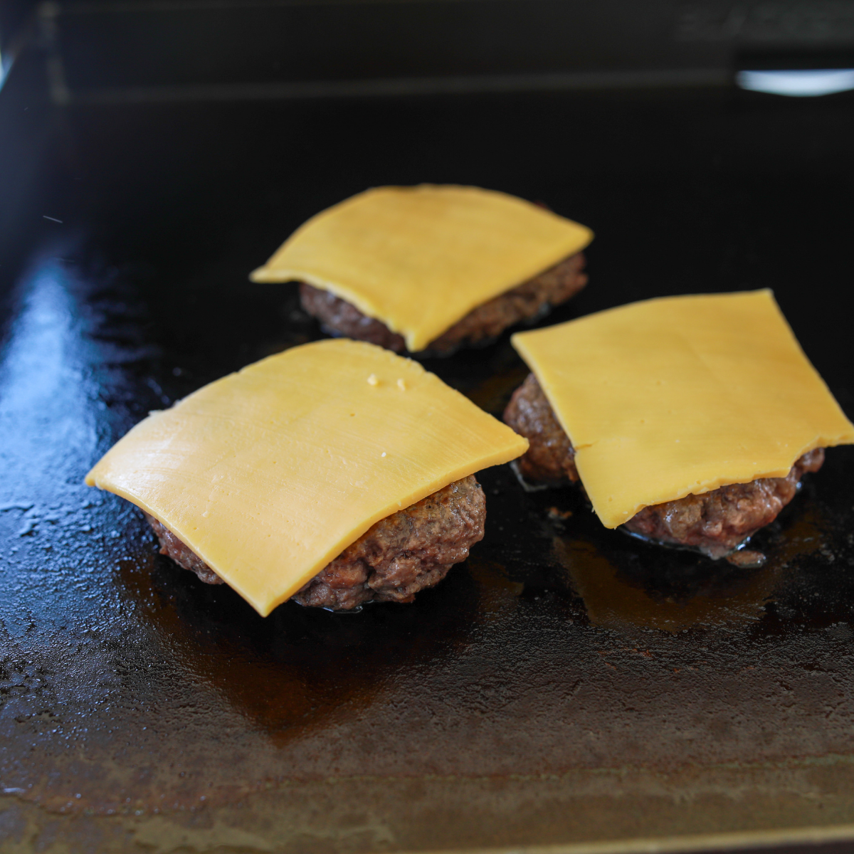 Ground beef ball being smashed into a thin patty on a Blackstone griddle using a burger press and parchment paper