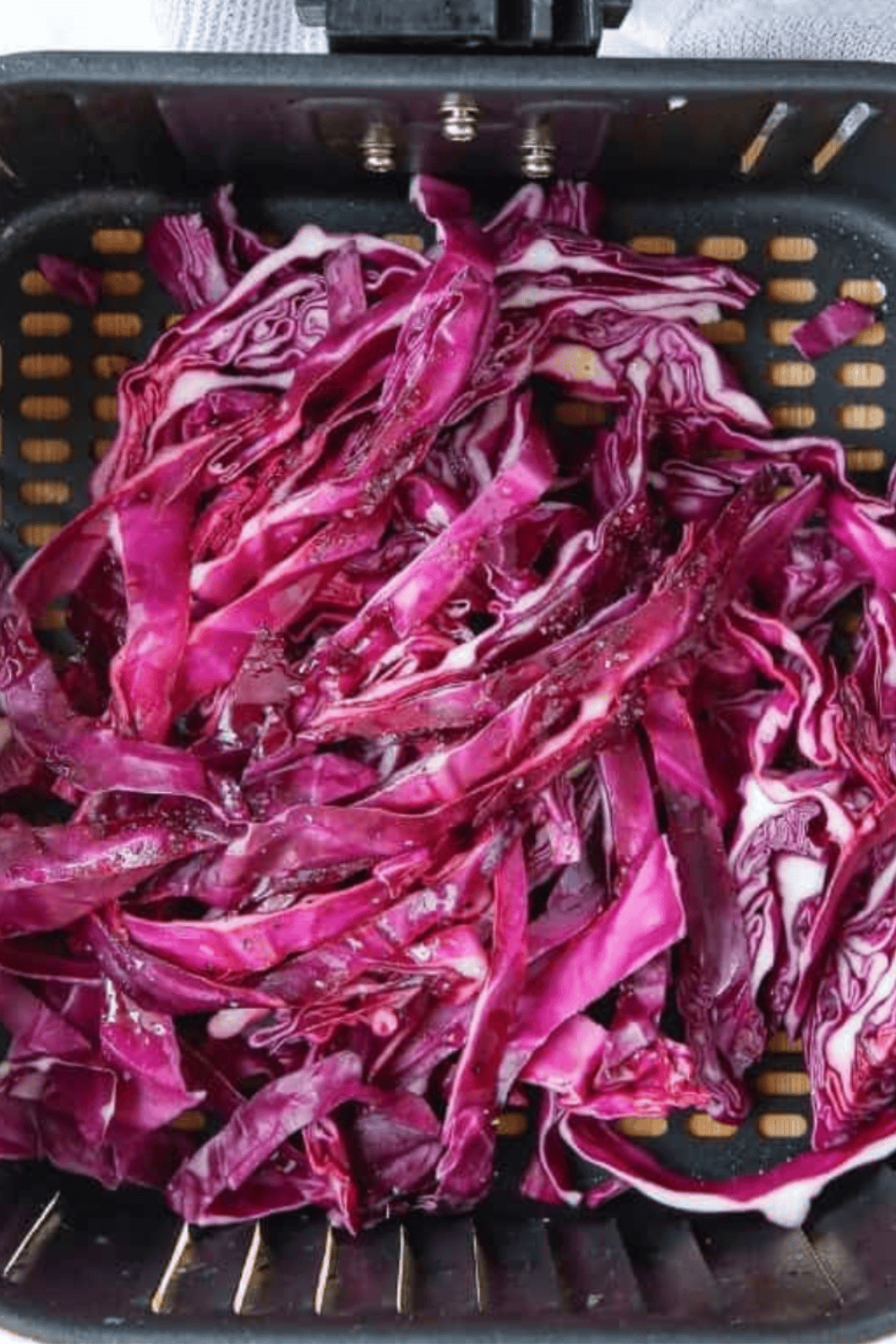 Air fryer basket filled with seasoned red cabbage pieces cooking, flipped halfway through for even crispiness.