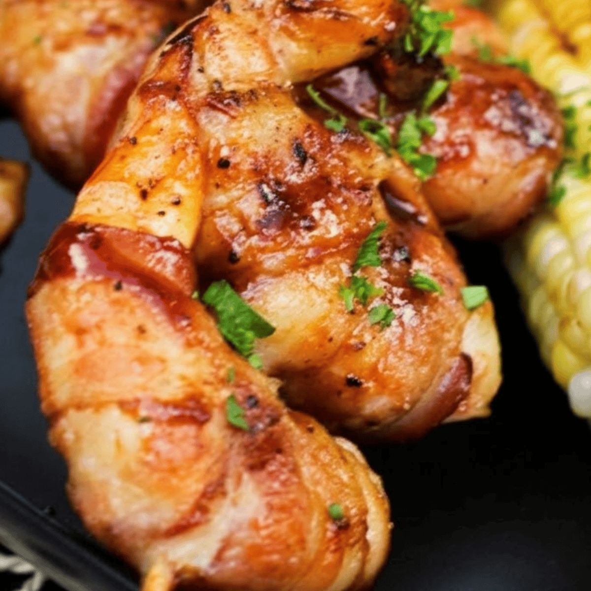 Bacon-wrapped BBQ shrimp on a platter, garnished with herbs and served with dipping sauce.