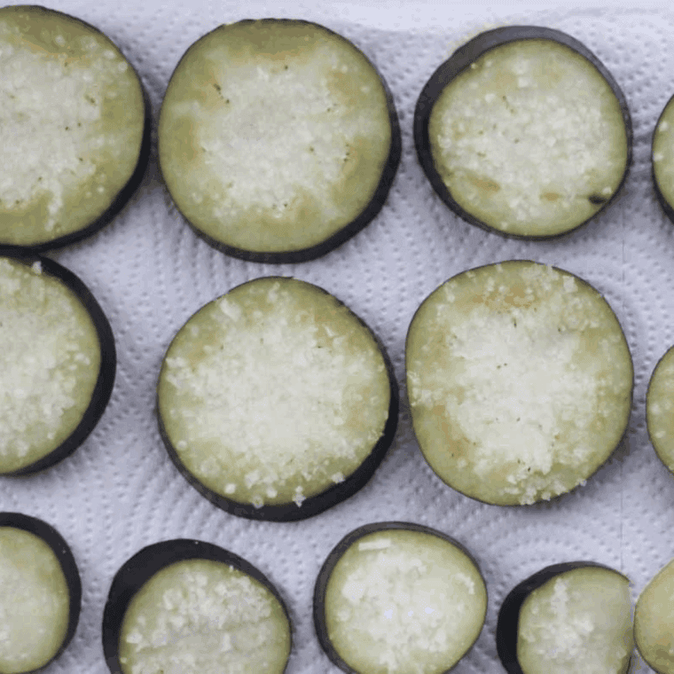 Salting sliced eggplant discs on a paper towel-lined baking sheet to remove moisture for air frying.