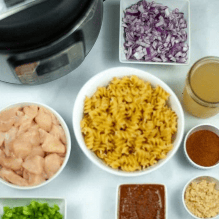 Ingredients for Instant Pot chicken fajita pasta laid out: chicken breasts, rotini, salsa, bell peppers, onion, fajita seasoning, heavy cream, shredded cheese.