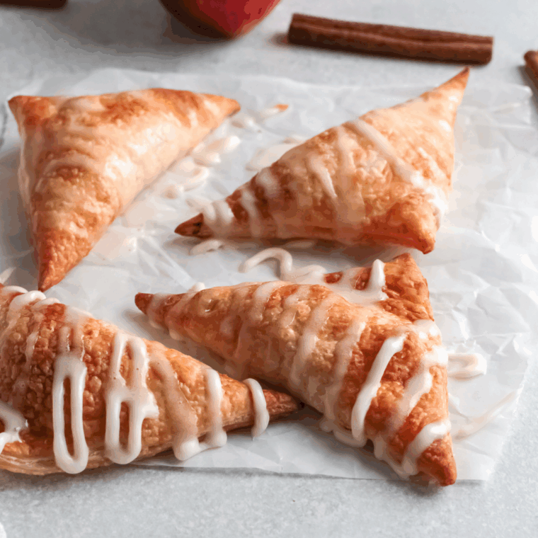 Golden air fryer apple turnovers stacked on a white plate, dusted with powdered sugar