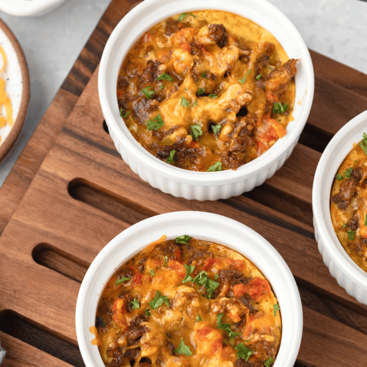 Overhead of individual air fryer breakfast casseroles in white ramekins topped with cheddar