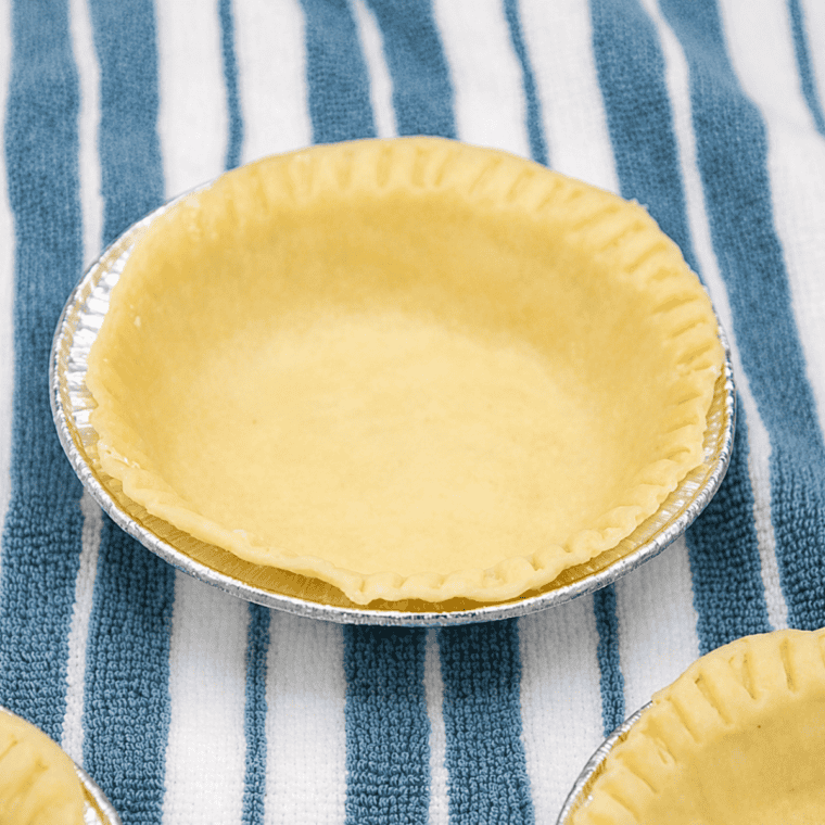 Pressing pie dough into the bottom and up the sides of mini pie pans for air fryer cherry crumb pie