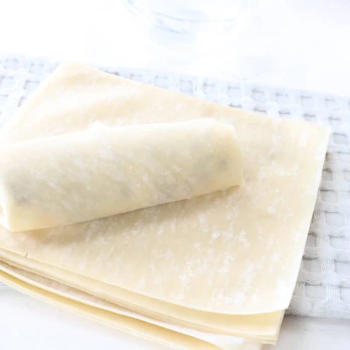 Pastry brush wetting the edges of an egg roll wrapper before folding it around the cookie dough