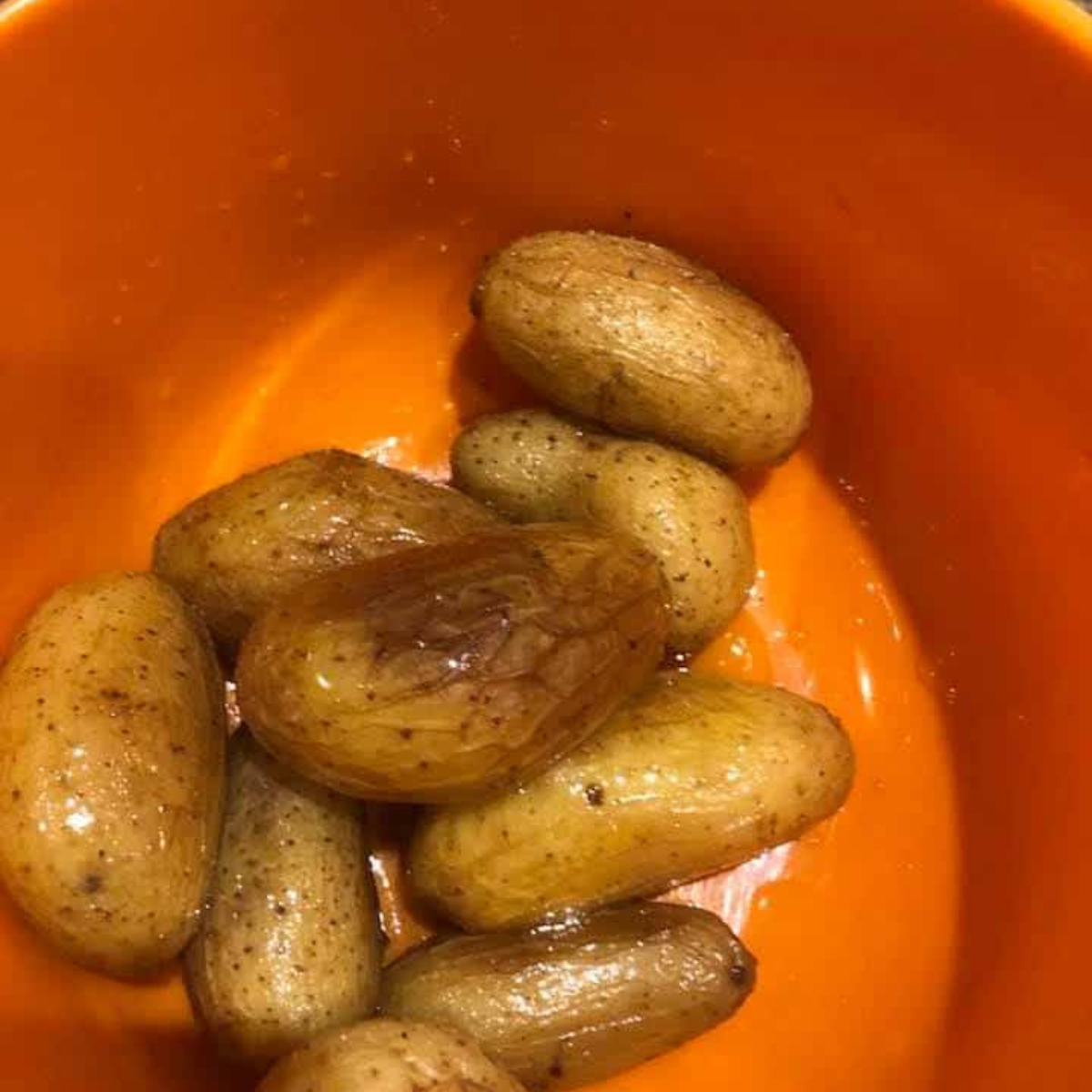 Whole fingerling potatoes tossed in olive oil and kosher salt in a large glass mixing bowl.