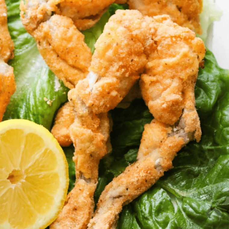 Golden-brown frog legs cooked in an air fryer, served on a plate with fresh herbs.
