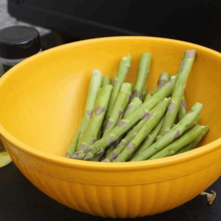 Asparagus tossed with olive oil, salt, and pepper in a mixing bow