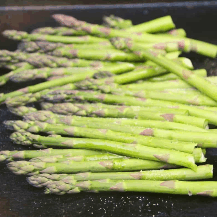 Seasoned asparagus spears placed in a single layer on a hot Blackstone griddle