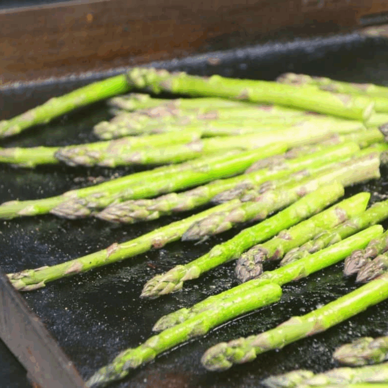 Asparagus being rolled with tongs to char evenly on the Blackstone